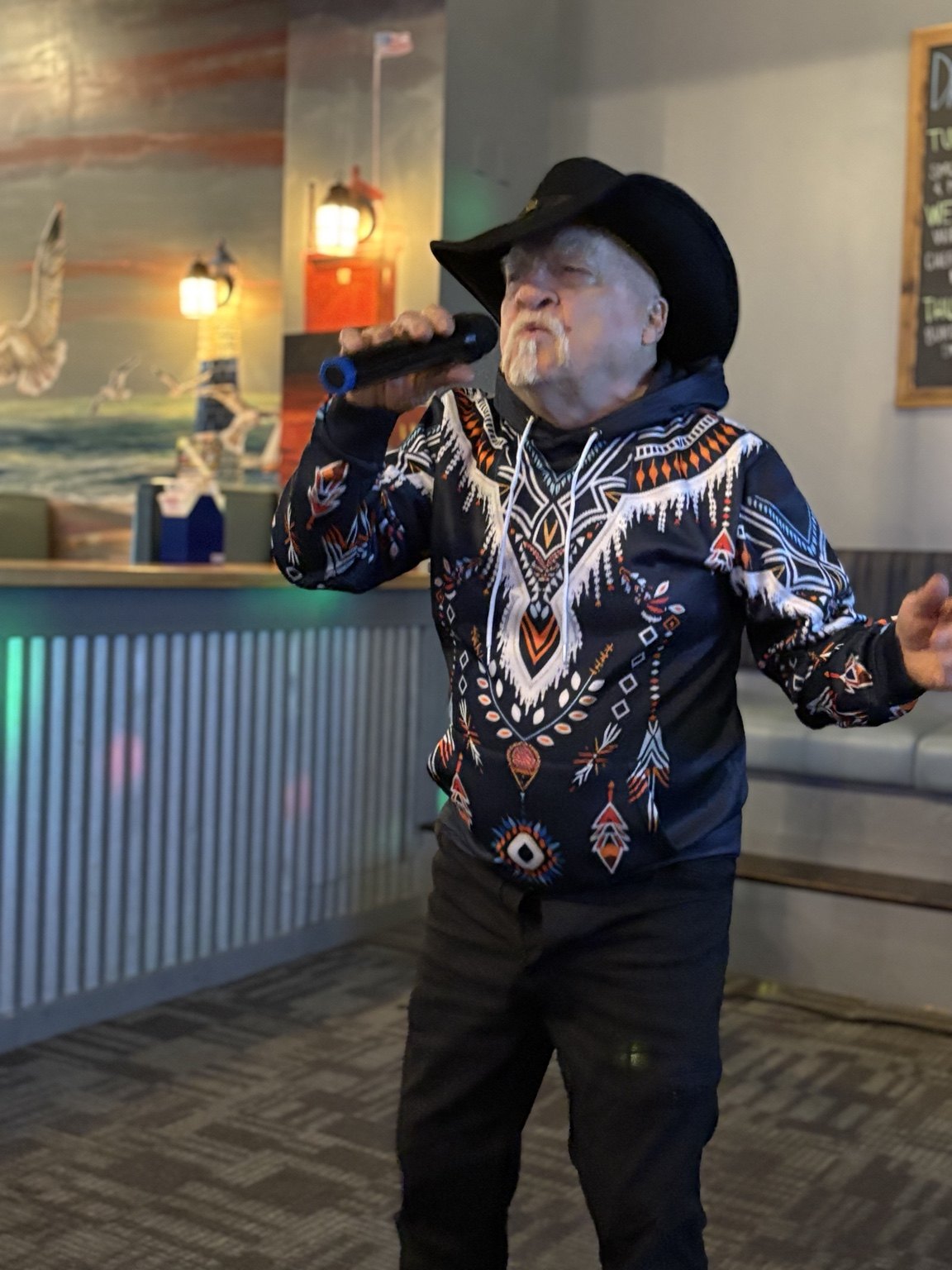 Karaoke singer wearing a cowboy hat and performing into a microphone beside the bar
