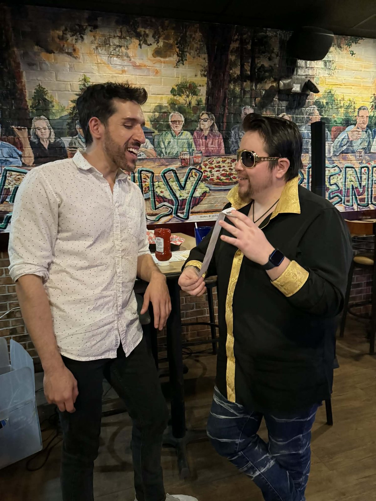 Two people smiling and sharing microphones at karaoke